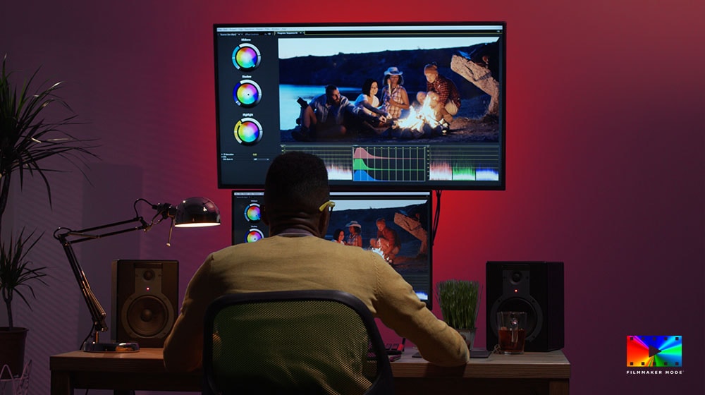 En filmskapare sitter vid ett skrivbord och använder två bildskärmar för att redigera färgerna i en video.
