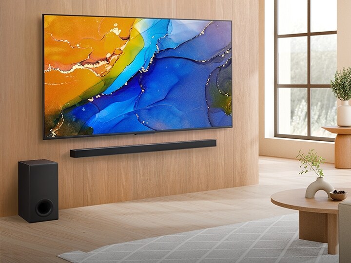 LG QNED TV mounted on a wall above a LG Soundbar in a modern living room space. LG QNED TV depicts a colorful abstract background.