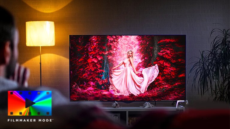 A man sitting on a sofa in the living room with the colofful movie on the TV screen