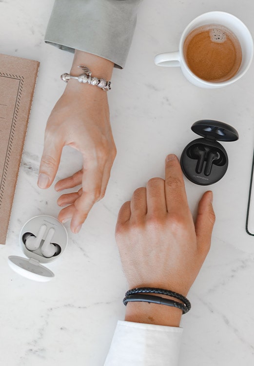 A man reaching out for the black earbuds and a woman reaching out for the white one