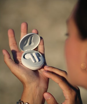 A woman looking at the earbuds while holding it on her hand