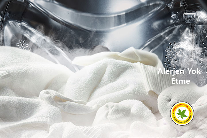 Çamaşır makinesinin tamburunda buharla kaplı yumuşak beyaz bir elbise ve peluş oyuncak gösterilir.