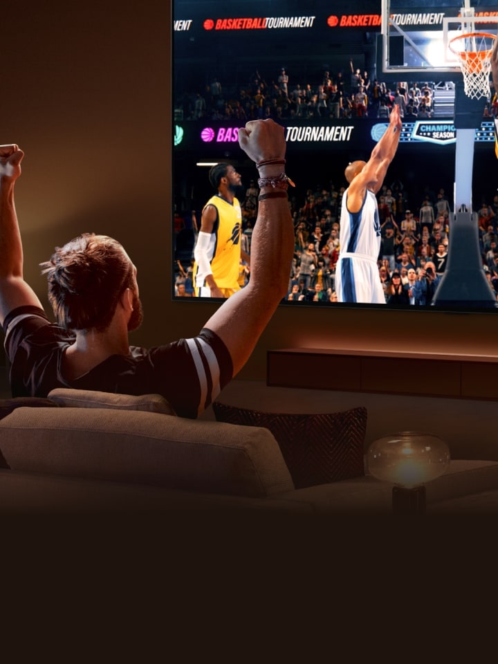 Ekranında basketbol oyunu görüntülenen ultra geniş LG TV’nin önünde koltukta oturan bir adam kolları havada tezahürat yapıyor.