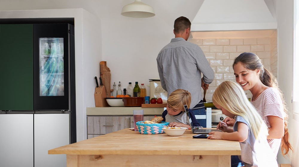 The whole family is sitting at the table preparing a meal. InstaView refrigerator installed on one side of the kitchen is creating cool air quickly.