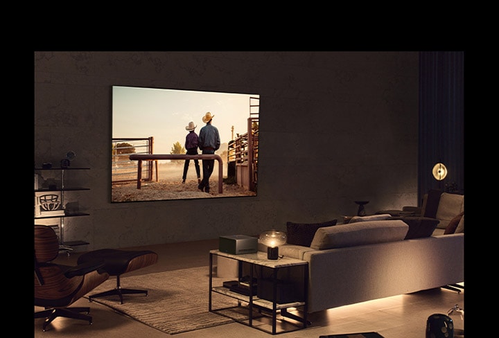 A man watching a cowboy movie with his dog in a cozy living space in the evening. There are no wires surrounding the wall-mounted LG OLED TV, and the Wireless Connect Box sits neatly on a side table. And then, the image slides to another image that shows a man watching a cowboy movie with the  LG OLED TV on a floor stand in a cozy and dark living space. There are no wires surrounding the LG OLED TV and its floor stand, and the Wireless Connect Box sits neatly on a side table.