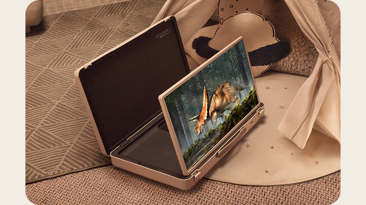 LG StanbyME Go case is opened up and the screen propped up. Two kids at home in a camping setup with a tent and warm, cozy lights. They are watching a video on the StanbyME Go screen.