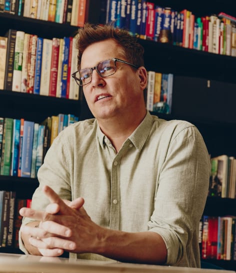 Man sitting in front of a bookshelf in a relaxed indoor setting