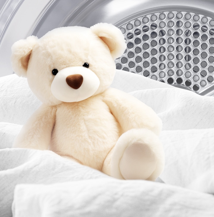Image of a clean teddy bear and white fabric inside a dryer drum.