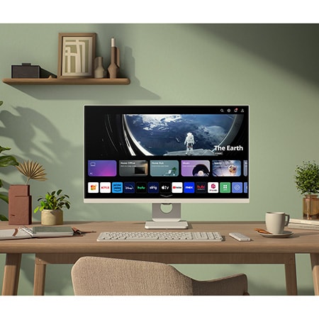 The LG Smart Monitor 27U511SA in a white finish, serving as a webOS Smart Hub, shows streaming apps for entertainment in a modern, plant-filled home office.