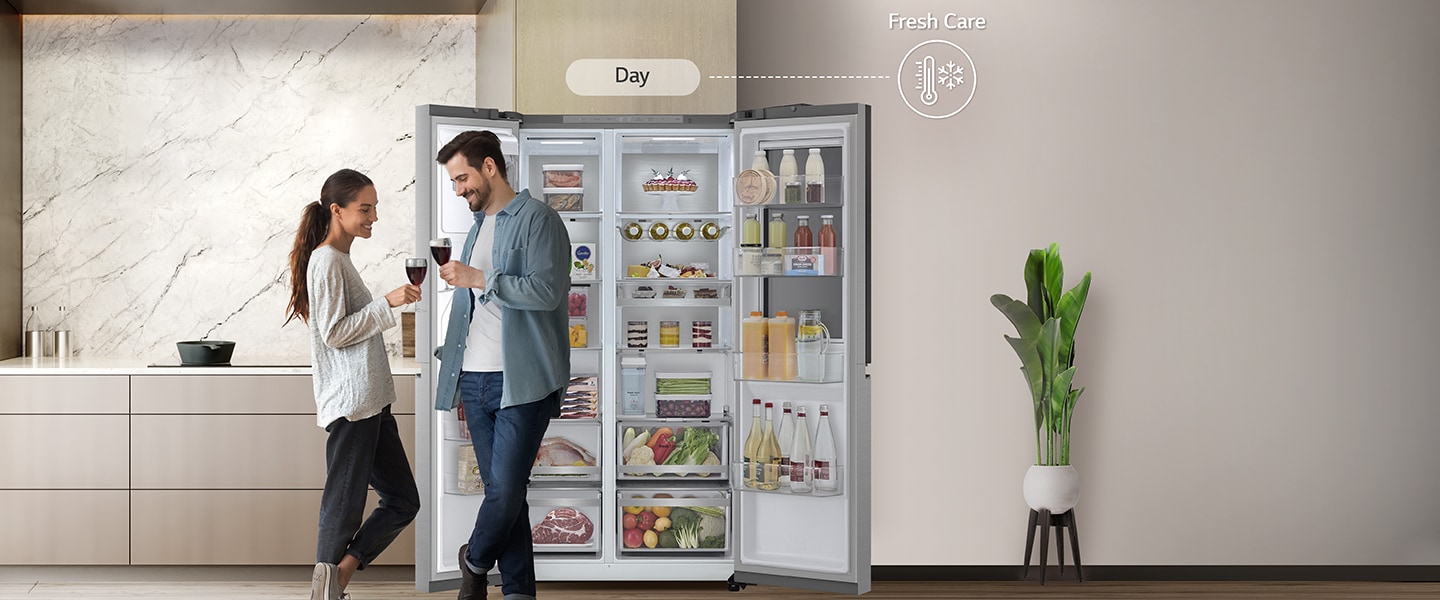 On the left side, The refrigerator is open and the couple is standing near the refrigerator.