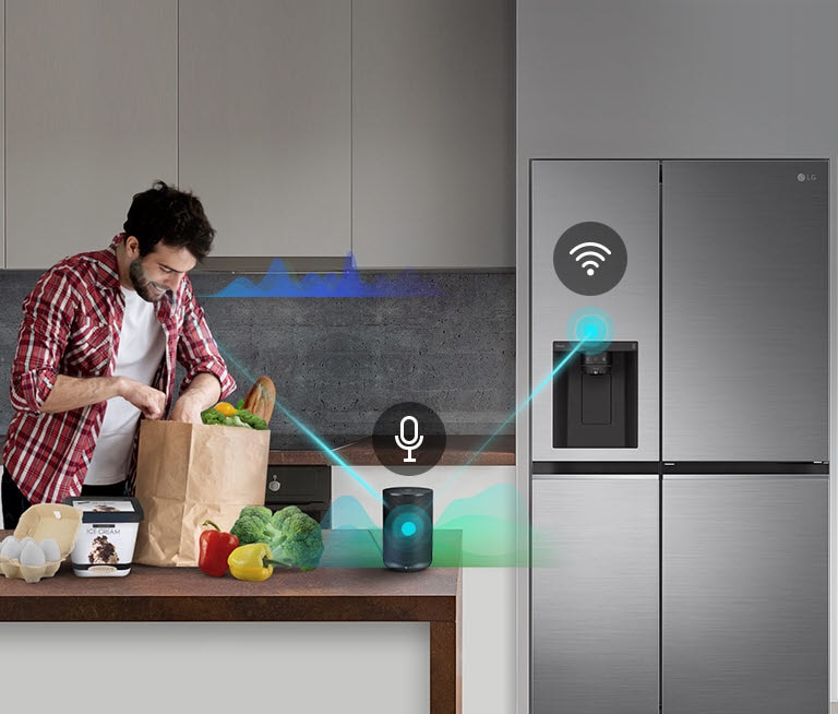 Man unpacks groceries in a kitchen with smart fridge, voice-activated device, and groceries on the counter.