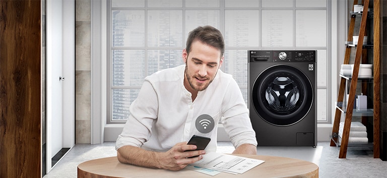 A man is monitoring the condition of the washing machine through a mobile phone app.