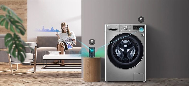 A woman sitting on the couch and drinking tea is giving orders to her washing machine through her AI speaker.