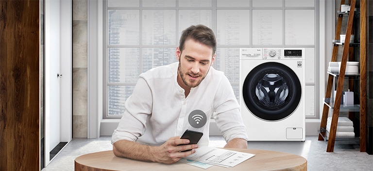 A man is monitoring the condition of the washing machine through a mobile phone app.