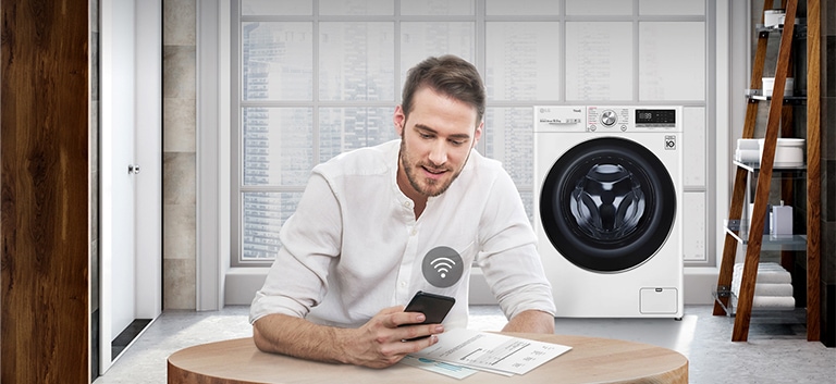 A man is monitoring the condition of the washing machine through a mobile phone app.