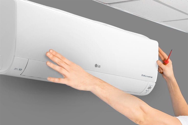 The side view of the air conditioner can be seen on the wall. Two hands are reaching up, one holding a tool, showing the ease of installation.