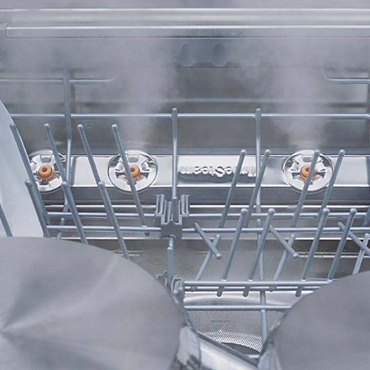 Footage of close-up view of various kinds of dishes being steam-washed inside dishwasher.