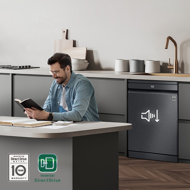 A man reading a book at the kitchen island while the LG free-standing Dishwasher is running in the background.