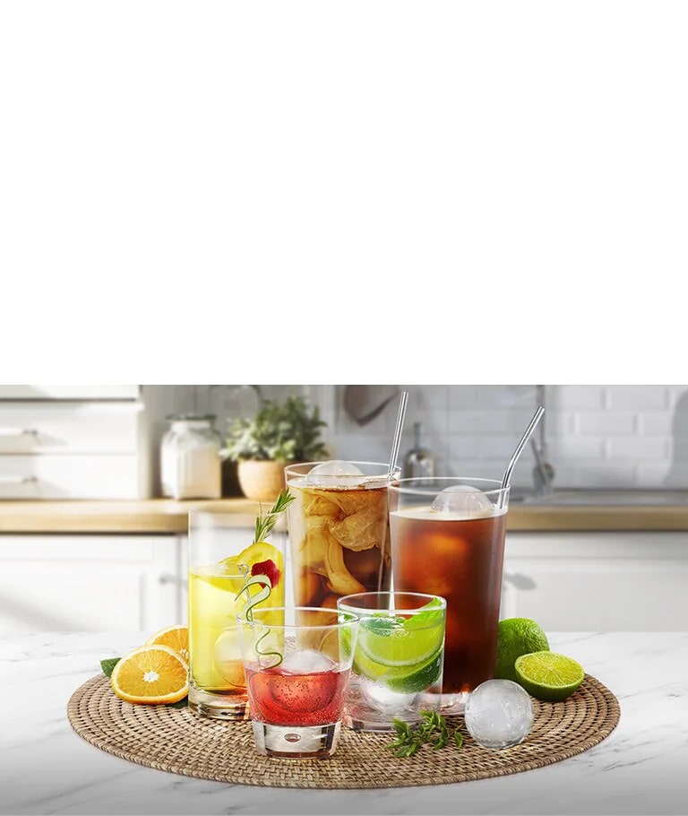 Various glasses of different sizes holding different drinks with round ice cubes are on a kitchen counter.