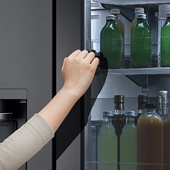 The front view of a black glass InstaView refrigerator with the light on inside. Hands tapping on InstaView screen.