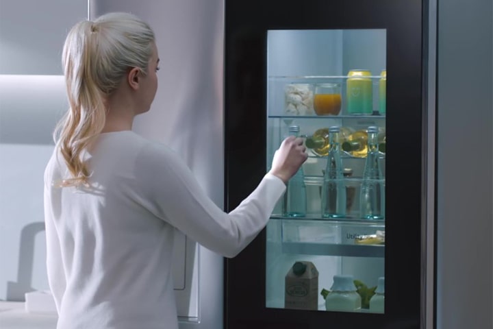 A video shows a woman approach her InstaView refrigerator and knock twice. The interior lights up and she can see the contents of her fridge without opening the door. The view zooms in to focus on the drinks in the door and then zooms out to see the woman from behind as she opens the door and grabs a drink.