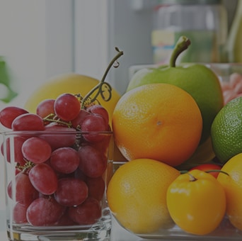 A glass of red grapes beside a bowl of citrus fruits, including oranges, lemons, and a lime, on a kitchen counter.