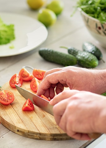 Image of cutting tomatoes on a cutting board with a knife.