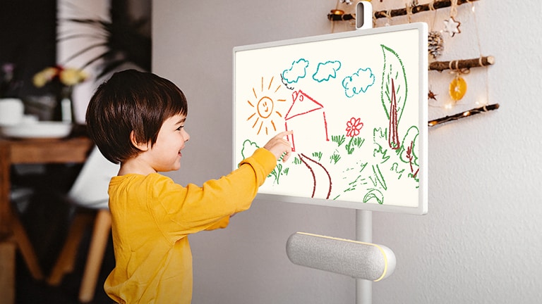 The LG StanbyME is placed in the kitchen with the XT7S speaker attached. A child draws on the screen, and the speaker's yellow mood lighting is on.