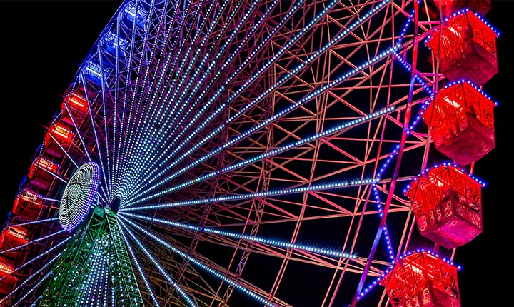 A slightly faded Ferris wheel illuminates at nighttime, with colored sparkles starting from the left side of the screen and moving across it. As the colored sparkles pass, the screen transitions from cloudy to bright, vivid colors.