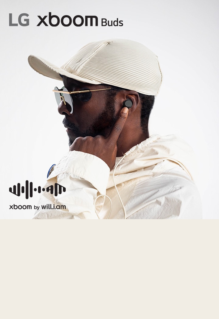 will.i.am in white outfit and sunglasses is his facing right side pointing the earbud in his ear with his left index finger.	