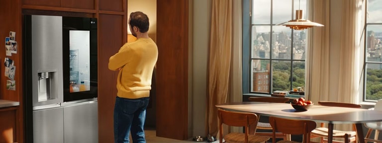  A man in a yellow jumper admires an LG fridge with a transparent panel, allowing him to see inside the fridge.