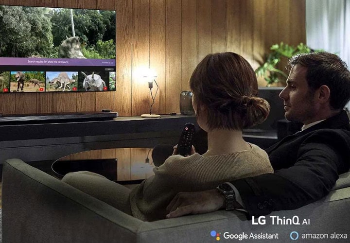 A couple relax as the LG OLED TV helps them choose their favourite photos to display, with the help of Amazon Alexa and the Google Assistant | More at LG MAGAZINE