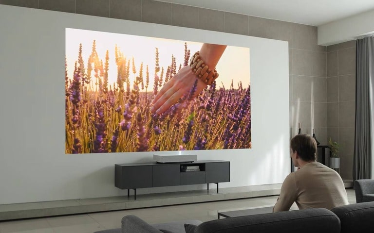 A spacious home theatre setup featuring a large projector screen displaying a serene field of lavender under a golden sunset, with a person sitting on a sofa enjoying the immersive viewing experience.