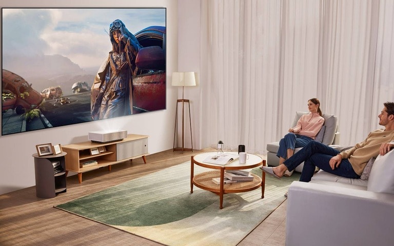 A couple relaxing in a modern living room, watching a large projection screen powered by an LG CineBeam projector placed on a wooden console below