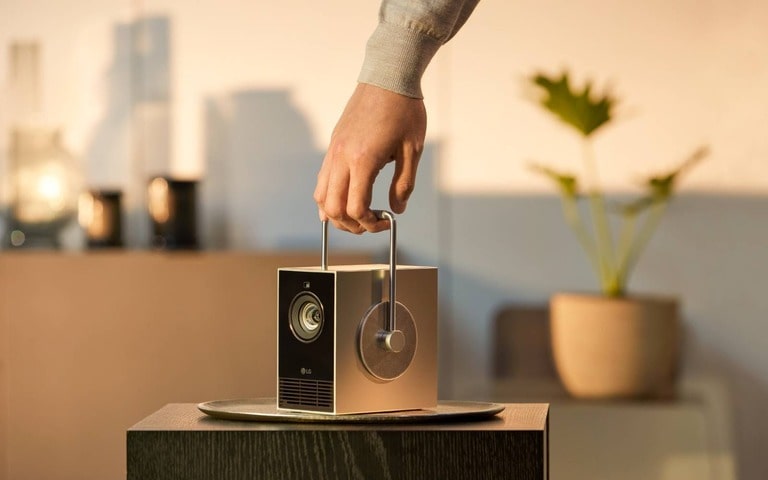 A person carrying a sleek and portable projector with a built-in handle, ready for easy setup, in a softly lit room with modern decor and minimalist design elements.