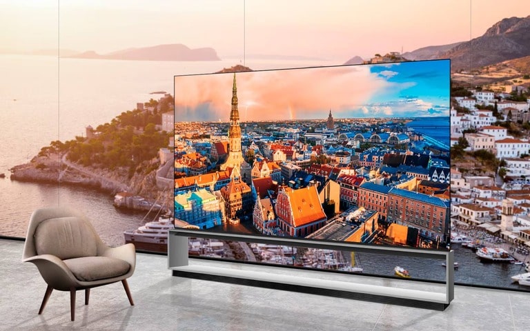 A modern living space featuring an LG TV displaying a vibrant cityscape with colorful rooftops and a tall spire, positioned next to a stylish armchair and overlooking a scenic coastal backdrop