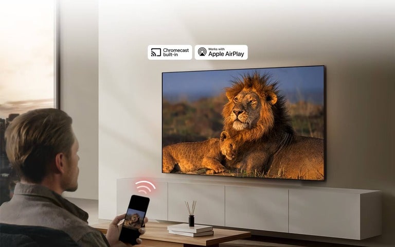 A person using a smartphone to cast a lion image onto an LG TV, showcasing Chromecast built-in and Apple AirPlay compatibility in a modern living room