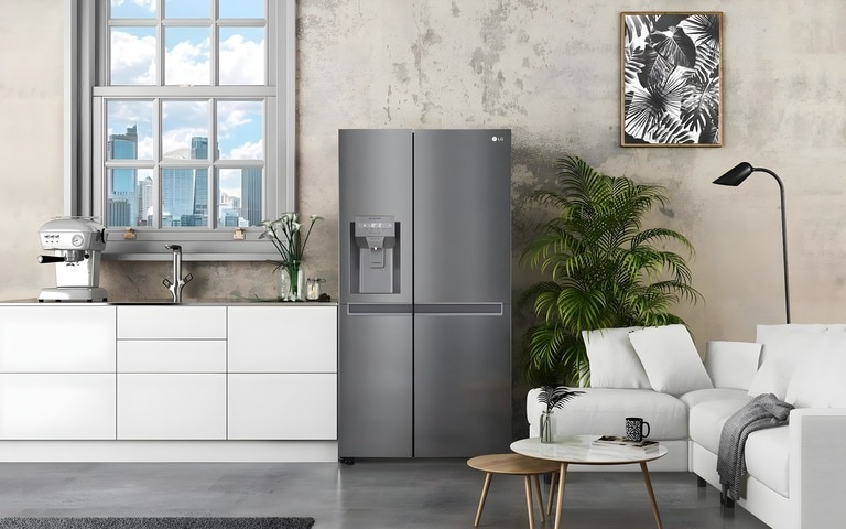 A modern kitchen and living area featuring an elegant stainless steel LG refrigerator, white cabinetry with a coffee machine, a large window with a city view, and a cozy white sofa accented by lush green plants and minimalist decor.