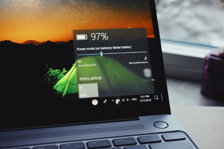 A laptop screen displaying a 97% battery status with power mode options, set against a sunset background wallpaper