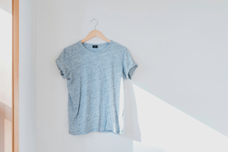 A light blue t-shirt hanging on a hanger against a white wall