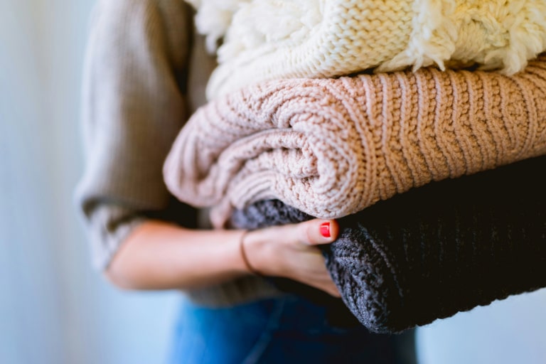 Person holding a stack of folded sweaters in various shades including cream, pink, and black