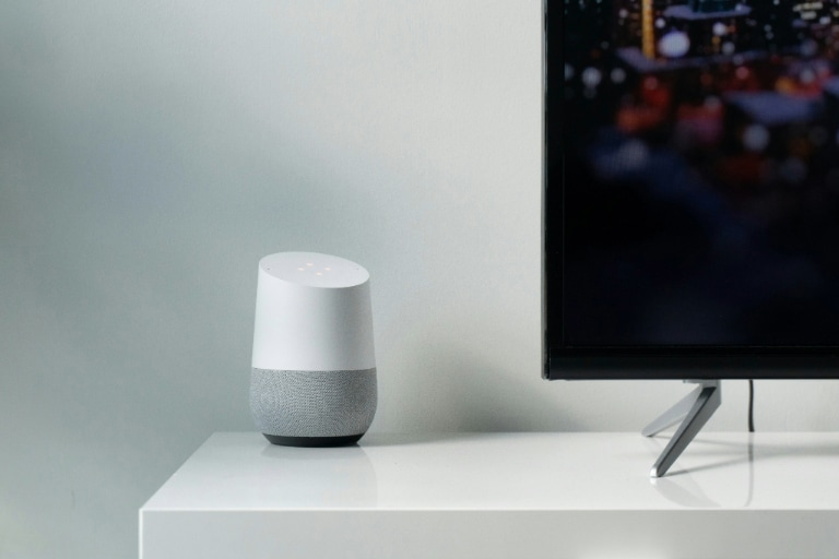 Smart Speaker on a white cabinet besides a flat screen television displaying a blurry cityscape