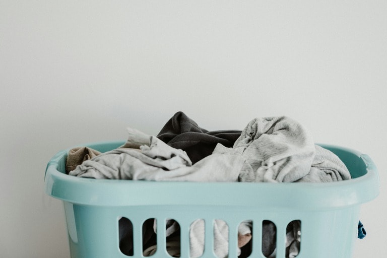 A light blue laundry basket filled with assorted clothes against a plain white background.