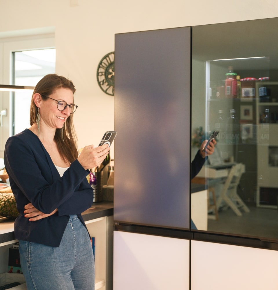 A woman uses the ThinQ app on her phone to play music via Bluetooth in front of the LG MoodUP Refrigerator.