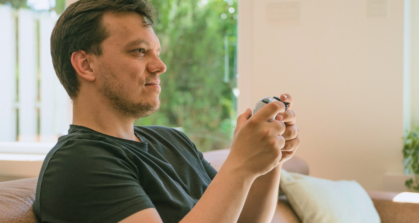 A relaxed gamer sitting on a couch, holding a game controller and looking focused.