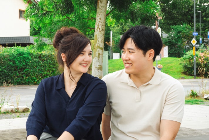 A couple sits together outdoors, smiling.