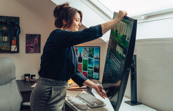 A woman adjusting a large vertical monitor in a home office.