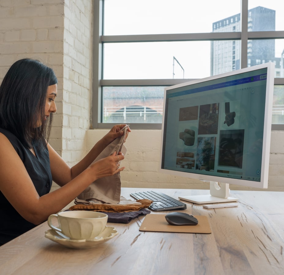 Lisa Mistry is sitting at her desk, working on an interior design project while touching fabric, with her LG MyView Smart Monitor.