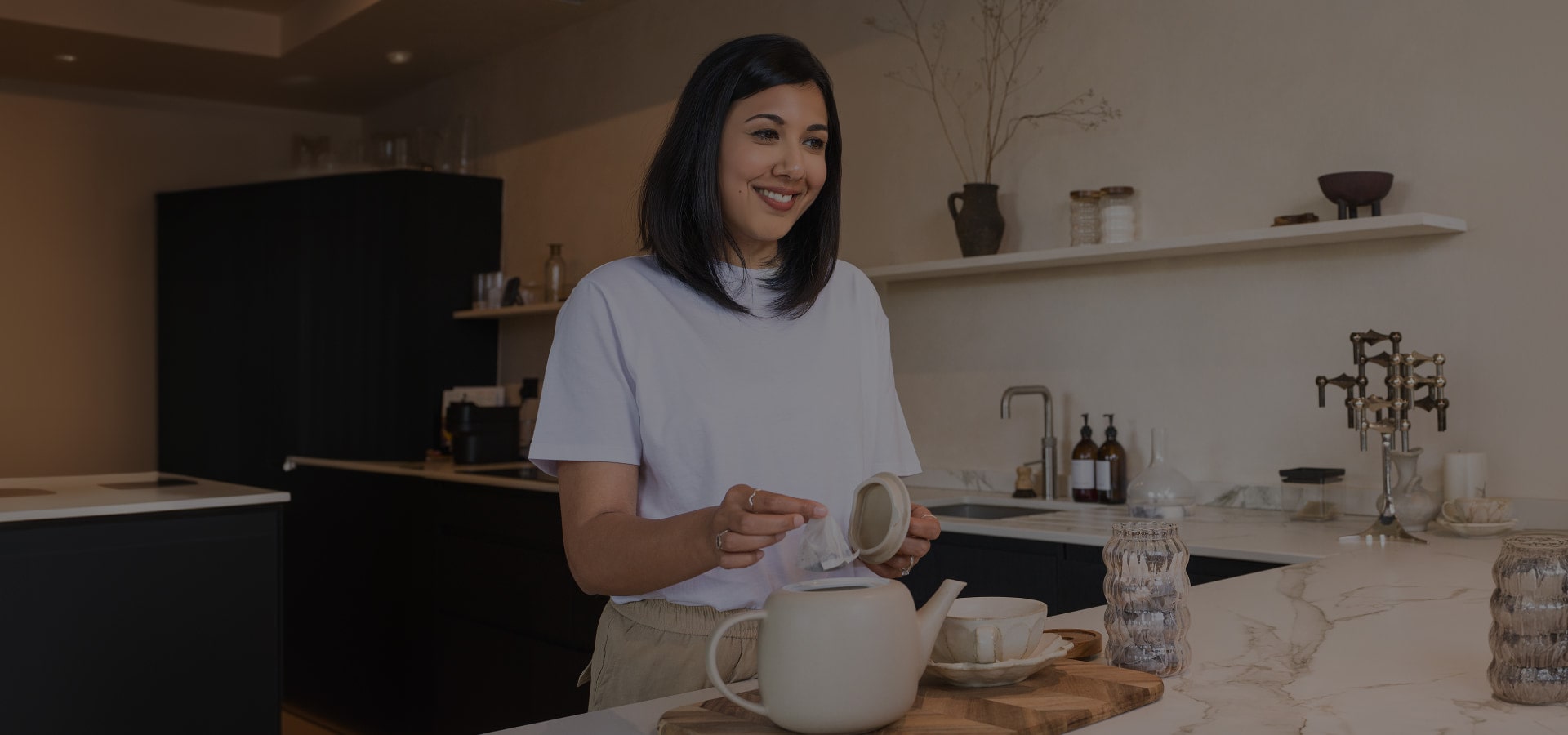 Lisa Mistry is smiling at the camera while placing a tea bag in the pot at the dining bar.