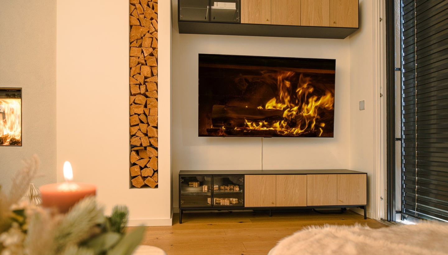 A cozy living room with an LG OLED TV showing a virtual fireplace, soft furnishings, and festive candlelight.